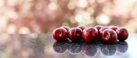 Fresh red cherries arranged in row on reflective surface with soft pink bokeh background for culinary and healthy eating concepts.