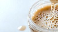 Close-up of fresh coffee being poured into glass mug with creamy foam and bubbles on white background for morning beverage and cafe concepts.