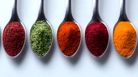 Vibrant colorful spices in silver spoons arranged in row showing sumac, dried herbs, paprika, chili and turmeric powder against white background for cooking and seasoning.