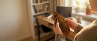 Empty wallet in hands showing financial hardship and money problems in cozy home office setting with warm lighting and wooden desk background.