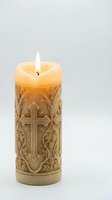 Ornate religious candle with carved cross and decorative floral patterns burning with bright flame on white background for spiritual ceremonies and worship.