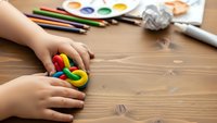 Child hands playing with colorful modeling clay on wooden table with art supplies. Creative kids activity for learning and development at home or school.
