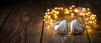 Two decorative silver hearts with warm golden fairy lights on rustic wooden background for romantic celebrations and holiday decor.