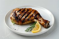 Grilled chicken leg quarter with crispy charred skin, fresh rosemary sprig and lemon wedge served on white plate against light background.
