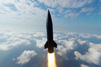 Missile launch above clouds with bright rocket engine flame, dramatic low angle view against blue sky and white cumulus cloudscape background.