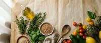 Fresh organic ingredients with herbs, vegetables, grains and olive oil arranged on rustic paper background for healthy cooking and meal preparation.