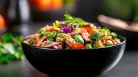 Fresh mixed salad with grilled beef strips, cherry tomatoes, herbs and vegetables in black bowl on kitchen counter for healthy dining and nutrition.