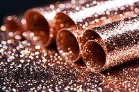 Metallic copper tubes with sparkling glitter scattered around on dark background, creating luxurious festive atmosphere. Macro photography with selective focus.