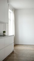 Minimalist kitchen interior with white cabinetry, granite countertop, potted succulent plant, tall window with sheer curtains, and wooden flooring. Bright, airy space ideal for home design and interior decoration projects.