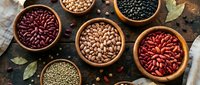 Assorted legumes and beans in wooden bowls on rustic surface. Variety of protein-rich pulses including kidney beans, black beans, and lentils for healthy cooking.