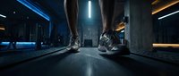 Two runners in athletic sneakers sprint toward camera on futuristic neon-lit urban pathway with blue and orange glowing lights, concrete architecture, and dark moody atmosphere for sports and technology concepts.