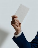 Professional in navy blue suit holding up blank white card against light background, demonstrating business presentation or showing document.