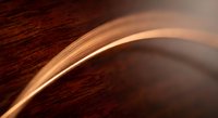 Elegant curved copper wire creating smooth flowing lines against rich wooden surface with warm lighting and shallow depth of field for modern design projects.