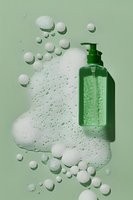Green plastic pump bottle with white foam bubbles and soap suds on mint green background, floating in creative composition for cosmetic and hygiene products.