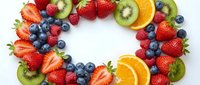 Colorful fresh fruit wreath with strawberries, blueberries, kiwi, orange slices and raspberries arranged in circle on white background for healthy eating concepts.