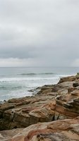 Rugged rocky coastline with layered stone formations meeting turbulent ocean waves under overcast sky, suitable for travel, nature, and environmental design projects.