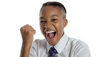 Young African American child in white shirt and tie celebrating with raised fist and excited expression against white background, conveying achievement and success.