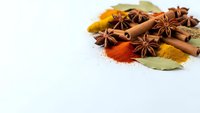 Aromatic spices including cinnamon sticks, star anise, bay leaves and colorful ground spices arranged on white background for culinary cooking recipes.