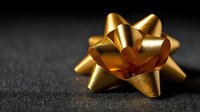 Golden gift bow on dark textured surface for luxury present wrapping and holiday celebration decoration.