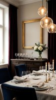 Elegant dining room with gold-framed mirror, amber glass pendant lights, dark wood sideboard, navy chairs, formal table setting, white flowers, and natural window light.