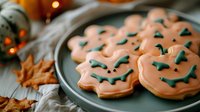 Festive Halloween sugar cookies decorated with orange icing and spooky jack o'lantern faces on gray ceramic plate with autumn leaves and holiday lights.