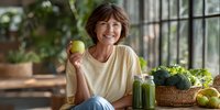 Middle-aged Caucasian woman holding green apple with fresh vegetables and smoothie in modern kitchen promoting healthy lifestyle and nutrition.