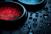 Red glowing powder in dark container with water droplets on black surface creates mysterious atmospheric macro photography composition.