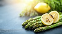 Fresh green asparagus spears and sliced lemons on dark background with soft natural lighting, raw organic produce for healthy cooking and food preparation.