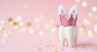 White tooth with pink glittery crown on soft pink background with golden bokeh lights. Dental care concept for children and fairy tale themes.