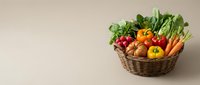 Fresh organic vegetables and fruits in wicker basket on neutral background for healthy eating and farm produce marketing materials.
