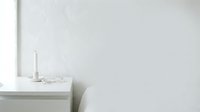 Minimalist white interior corner with shelf, candle, and books against blank wall space for design projects.