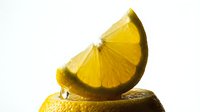 Fresh lemon slice balanced on a whole lemon with a juice drop, vibrant yellow citrus fruit on white background for food and drink design.