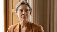 Confident mature businesswoman with gray hair in professional brown suit standing in elegant office interior for corporate leadership concepts.