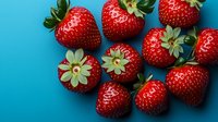 Fresh ripe strawberries scattered on vibrant blue background, showcasing bright red color and natural green leaves. Food photography for healthy eating concepts.
