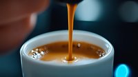 Fresh espresso coffee pouring into white ceramic cup with rich golden crema foam in modern cafe setting for morning beverage and caffeine concepts.