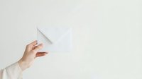 Close-up of a woman's hand holding a blank white envelope against a neutral background, suitable for business communication and mail concepts.