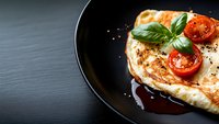 Grilled chicken breast with cherry tomatoes and fresh basil leaves on black plate, drizzled with balsamic reduction. Dark moody food photography.