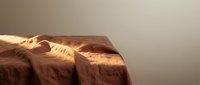 Crumpled brown linen fabric with warm sunlight casting dramatic shadows, suitable for textile, fashion, and interior design backgrounds.
