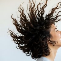 Young woman with curly dark hair in dynamic motion against white background. Hair care, beauty salon, natural texture concept for advertising campaigns.