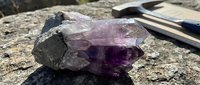 Raw amethyst crystal specimen with purple quartz formation on rock surface with geological tools for mineral collection and identification studies.