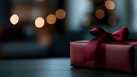 Elegant burgundy gift box with satin bow on dark surface against blurred bokeh lights background, creating romantic holiday atmosphere.