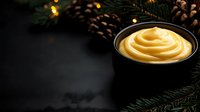 Creamy swirled custard or pudding in black bowl with festive pine cones and evergreen branches creating cozy holiday atmosphere on dark background.