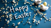Happy Easter text with decorative spring blossoms and yellow chick ornaments on dark blue background, festive holiday greeting card composition.