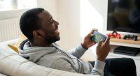 Young African American man relaxing on couch playing mobile video games at home, casual gaming lifestyle and entertainment technology.