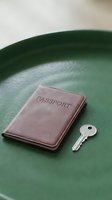 Burgundy leather passport holder and silver key on green tray, representing travel security, document protection, and journey planning for tourism and vacation concepts.