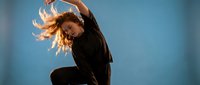 Young woman dancer performing expressive contemporary dance movement with flowing hair against blue studio background for artistic projects.