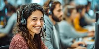 Smiling young Hispanic woman with headset working in customer service call center with colleagues in background.