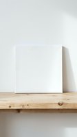 Blank white canvas frame on wooden shelf against neutral wall for art display and creative projects.