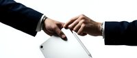 Two businessmen in suits exchanging a digital tablet and stylus pen, symbolizing partnership, deal, or technology transfer in a corporate setting.