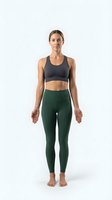 Athletic woman with medium skin tone wearing dark gray sports bra and forest green leggings, standing in neutral pose against white background for fitness and wellness marketing.